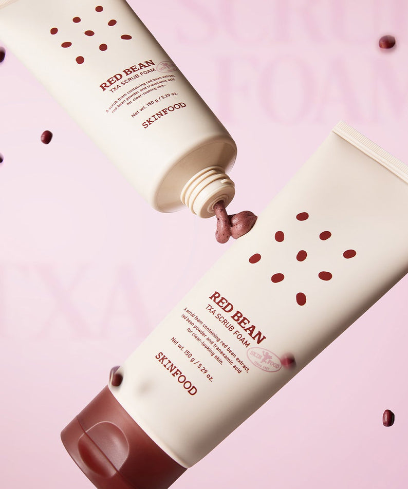 SKINFOOD Red Bean Tranexamic Acid Scrub Foam 150g de SKINFOOD sur fond rose, tubes entre des grains de haricot rouges