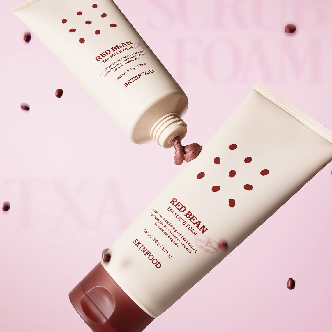 SKINFOOD Red Bean Tranexamic Acid Scrub Foam 150g de SKINFOOD sur fond rose, tubes entre des grains de haricot rouges