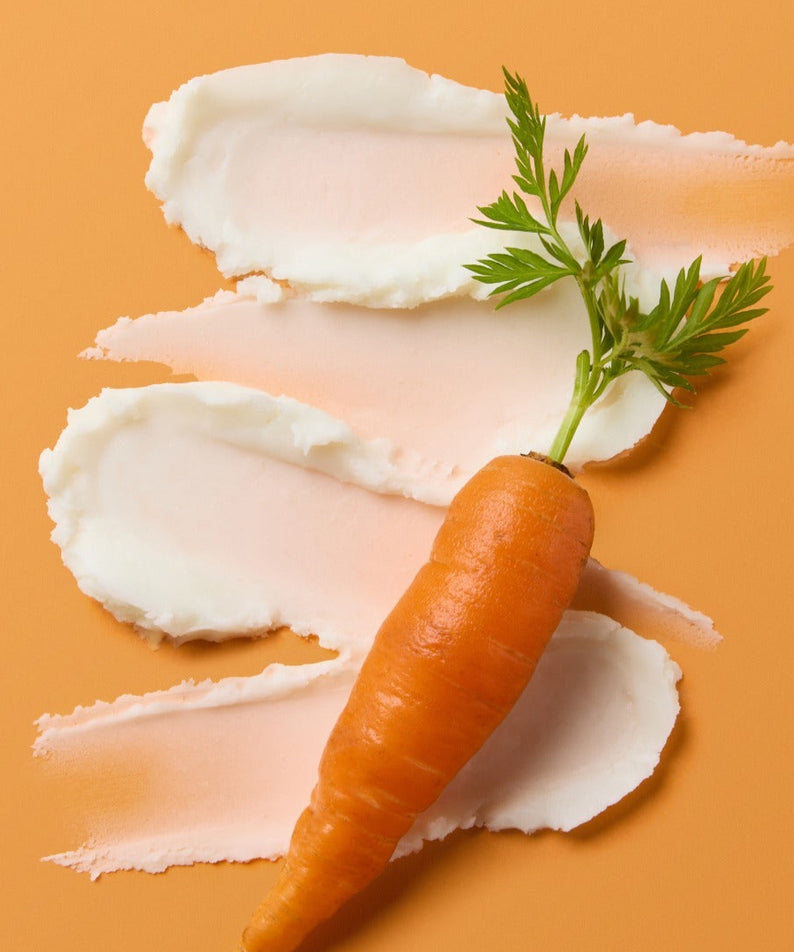 Texture du SKINFOOD Carrot Airy Soft Sun Stick 18.5g avec carotte fraîche posée sur fond orange.