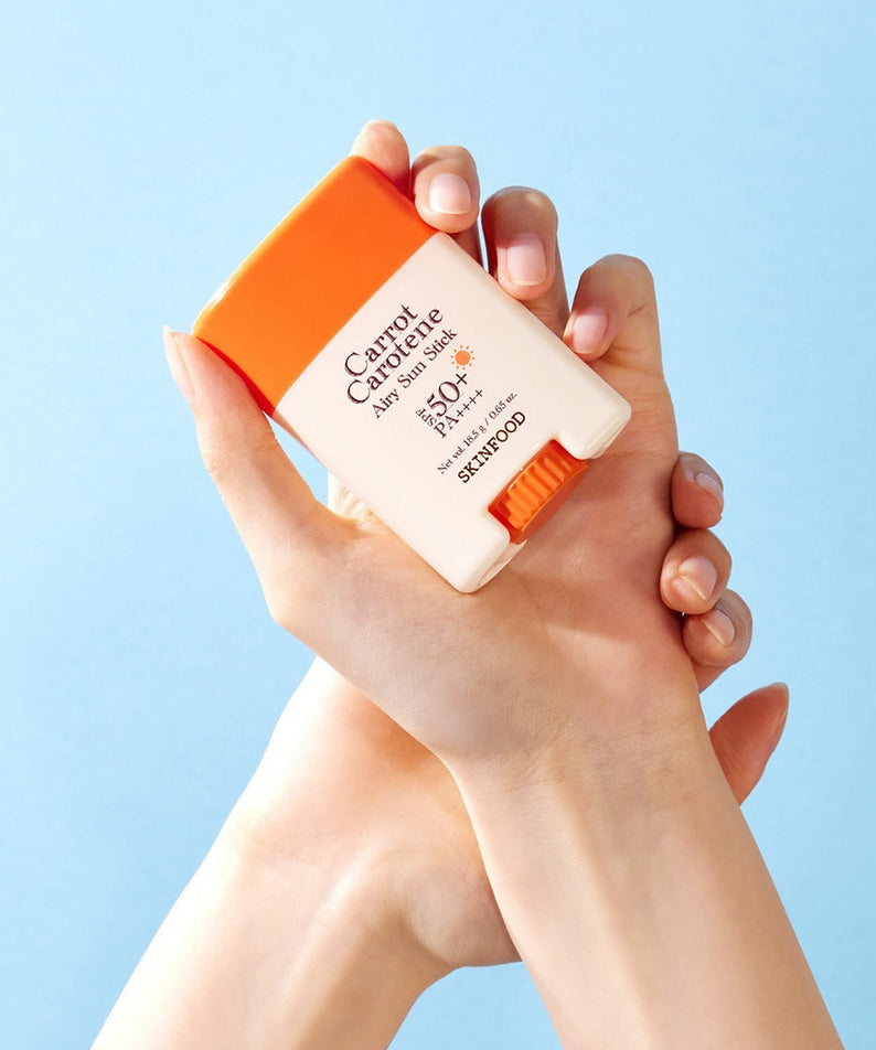 SKINFOOD [NEW] Carrot Airy Soft Sun Stick (18.5g) tenu en main, crème solaire en stick avec protection SPF, fond bleu ciel