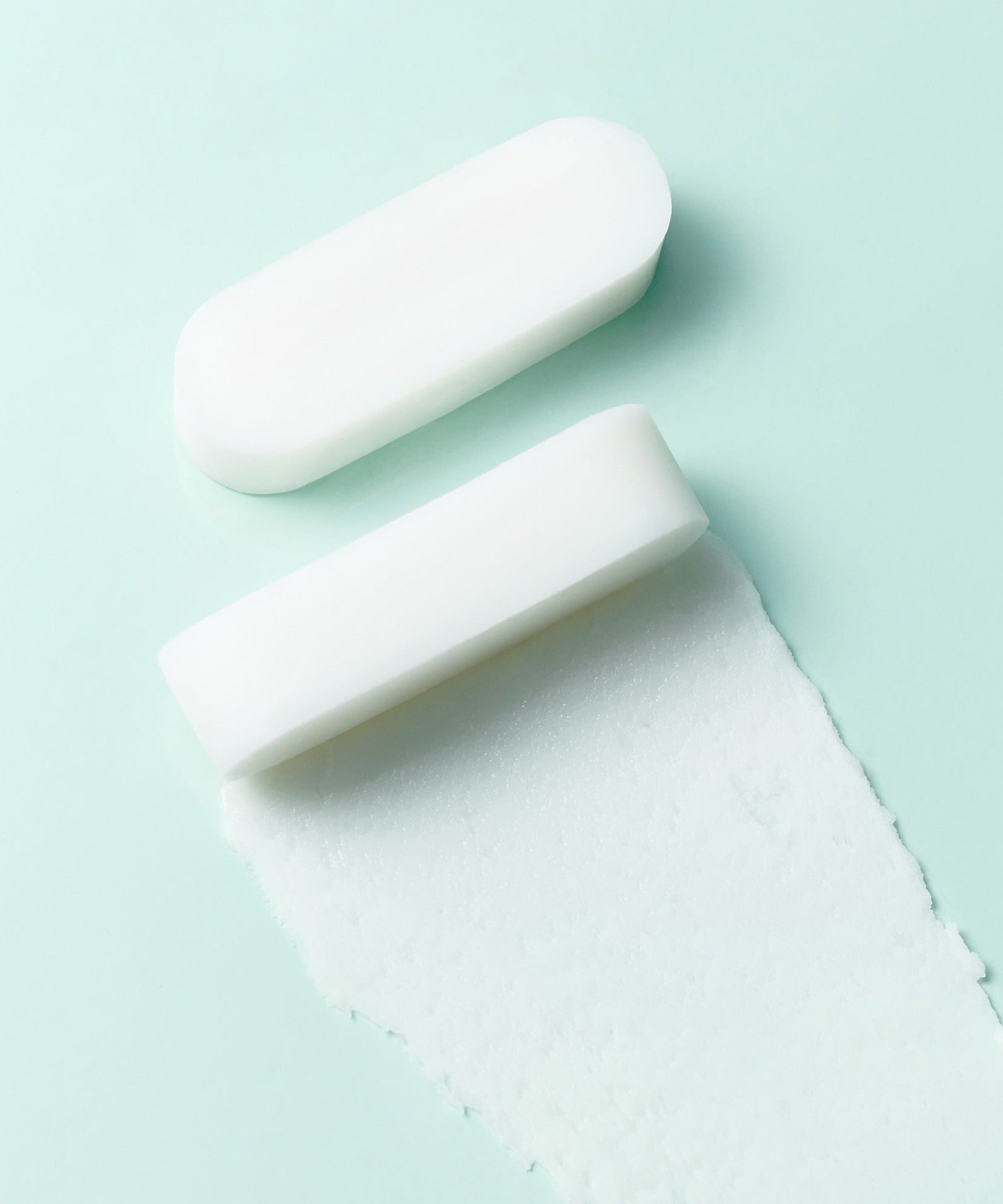 Barre de savon blanc sur fond vert clair avec une trace douce, minimaliste et apaisant.