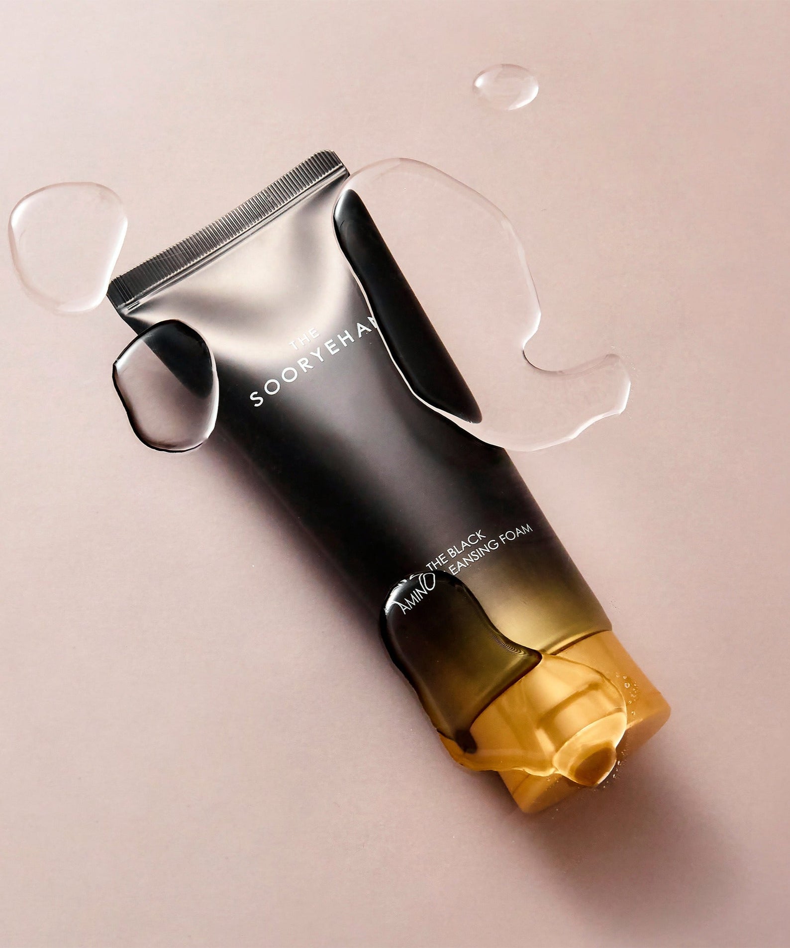 SOORYEHAN The Black Amino Cleansing Foam 150ml, marque SOORYEHAN, flacon noir sur fond beige avec gouttes d'eau.