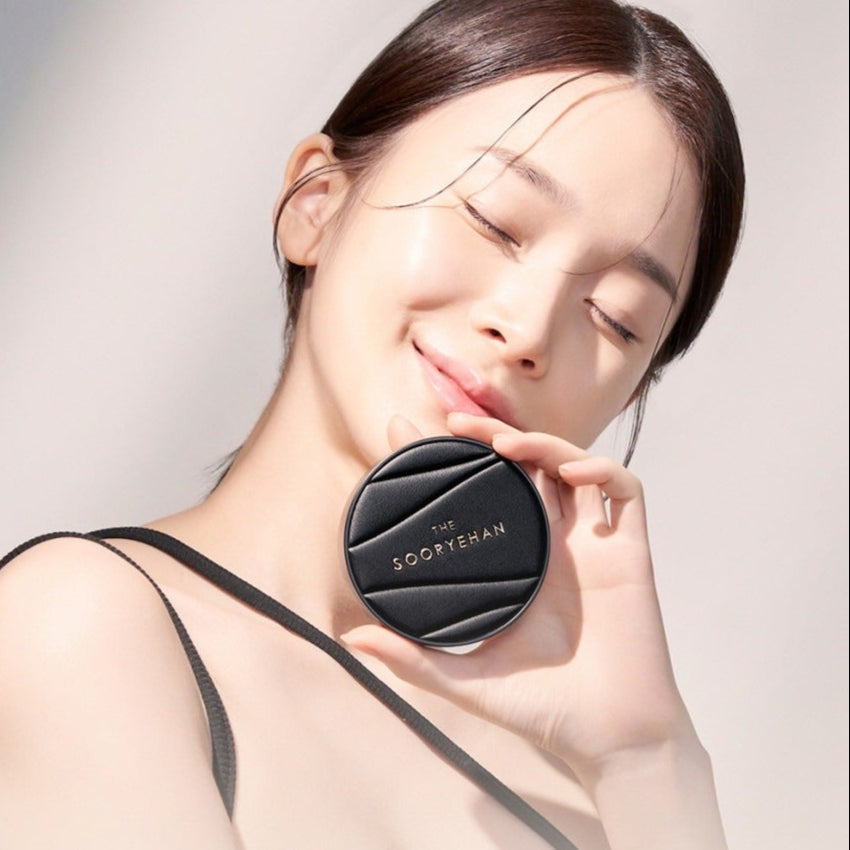 SOORYEHAN The Black Tension Fit Mesh Cushion 13g : femme lissant son visage, packaging noir sur la peau, fond clair.