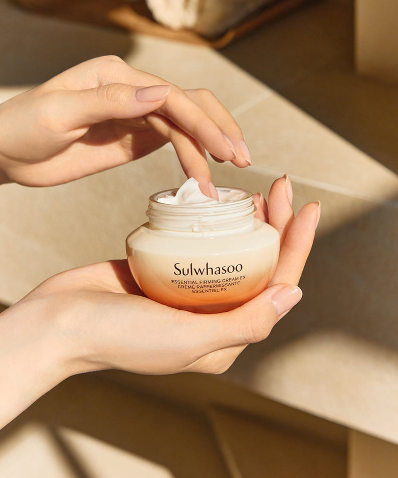 Décris l'image en français: SULWHASOO Essential Comfort Firming Cream 75ml, pot crème sur mains avec texture crème, décor salle de bain.