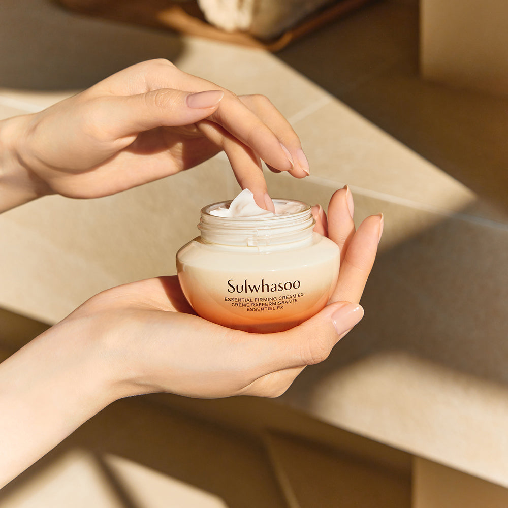 Décris l'image en français: SULWHASOO Essential Comfort Firming Cream 75ml, pot crème sur mains avec texture crème, décor salle de bain.