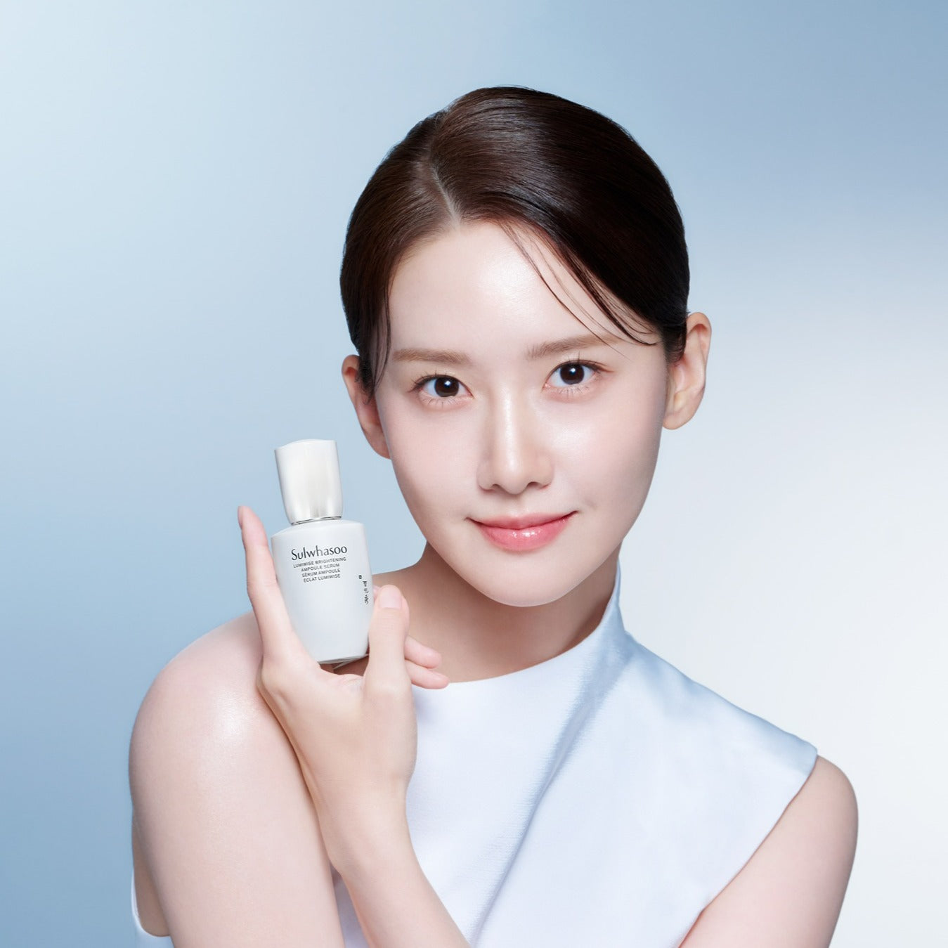SULWHASOO Lumiwise Brightening Ampoule Serum 30ml par Sulwhasoo, flacon blanc tenu par une femme sur fond bleu.