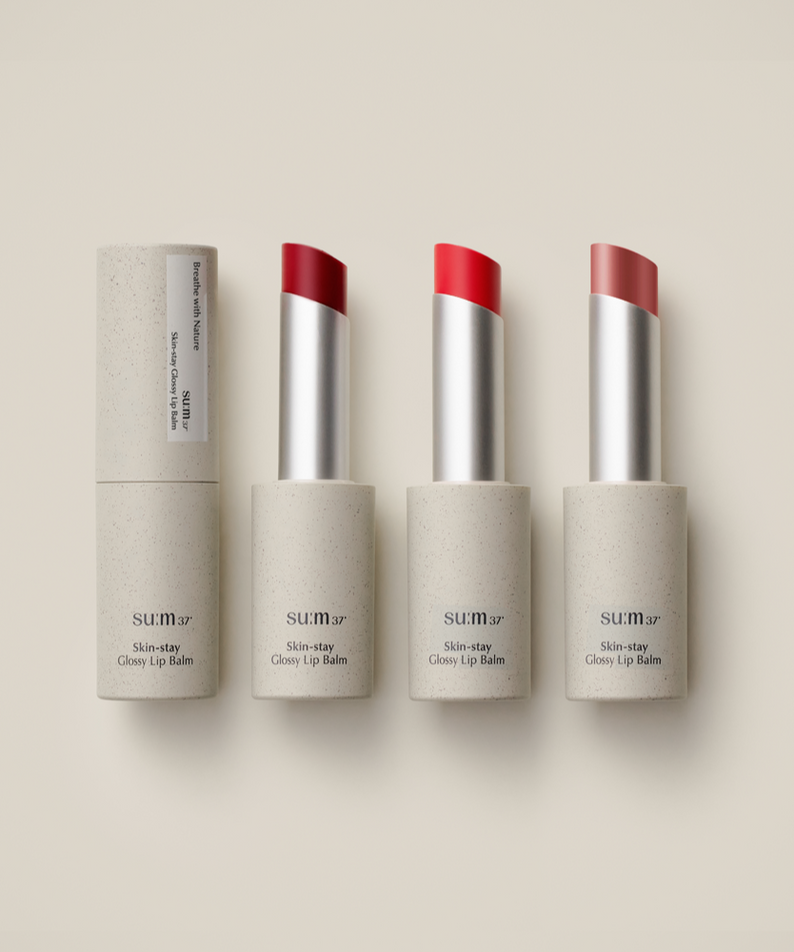 Baume à lèvres SU:M37 Skin-Stay Glossy avec trois teintes vives sur fond beige élégant.