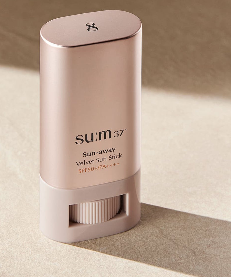 SU:M37 Sun-Away Velvet Sun Stick 18g en bâton sur une surface sableuse.