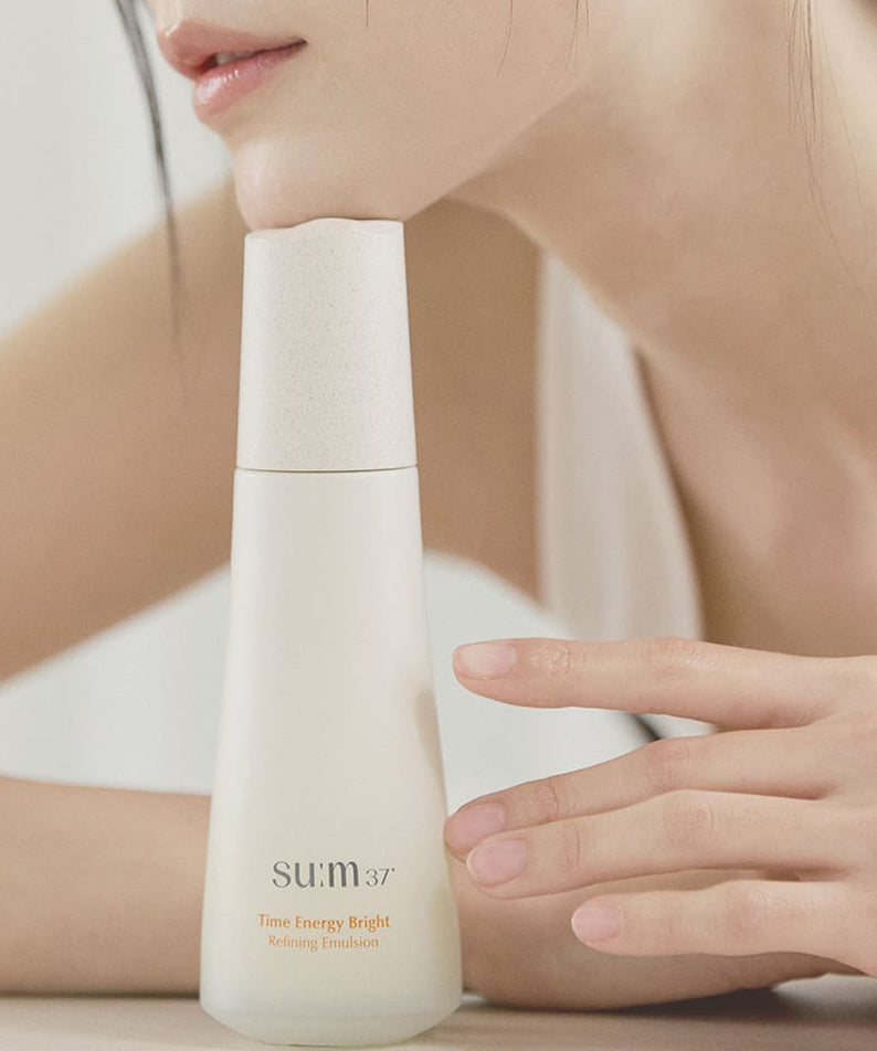 Femme posant avec SU:M37 Time Energy Bright Refining Emulsion 120ml, soin lumineux et raffiné pour la peau, flacon élégant.