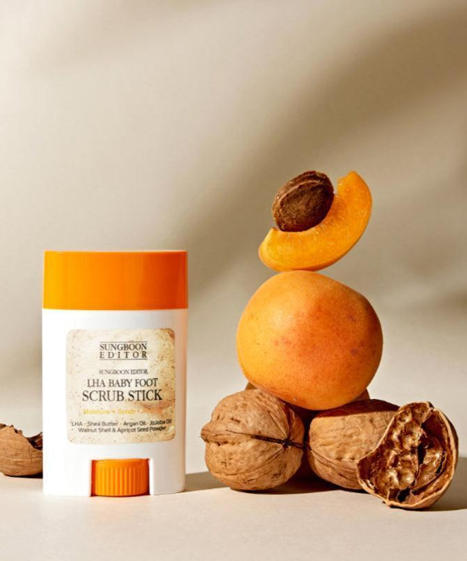 SUNGBOON EDITOR Laha Baby Foot Scrub Stick, pot orange sur fond beige avec abricots et noix, contexte spa.