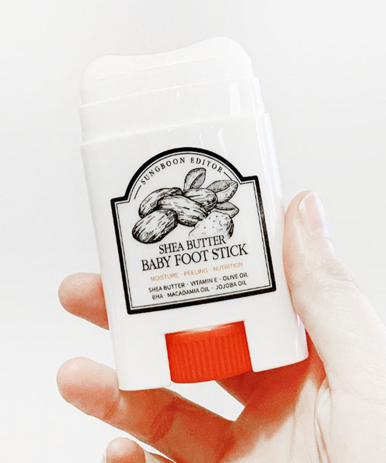 SUNGBOON EDITOR Shea Butter Baby Foot Stick : stick au beurre de karité, main tenant le produit sur fond blanc.