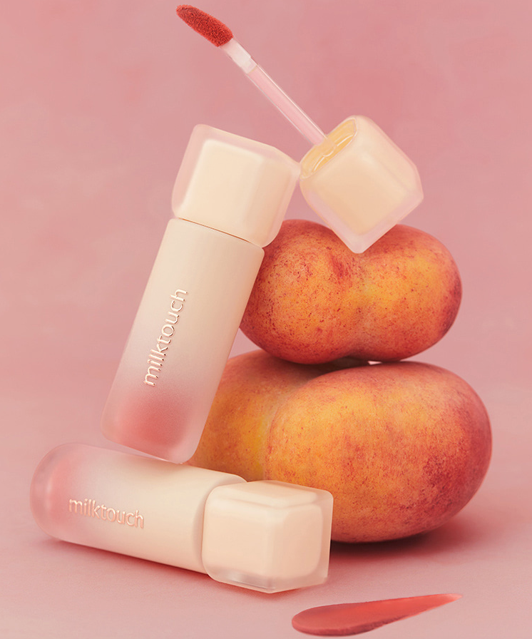 MILK TOUCH Spread Fit Blur Tint avec fruits en fond rose, cosmétique emballé sur fond de pêches, couleur douce et attrayante.