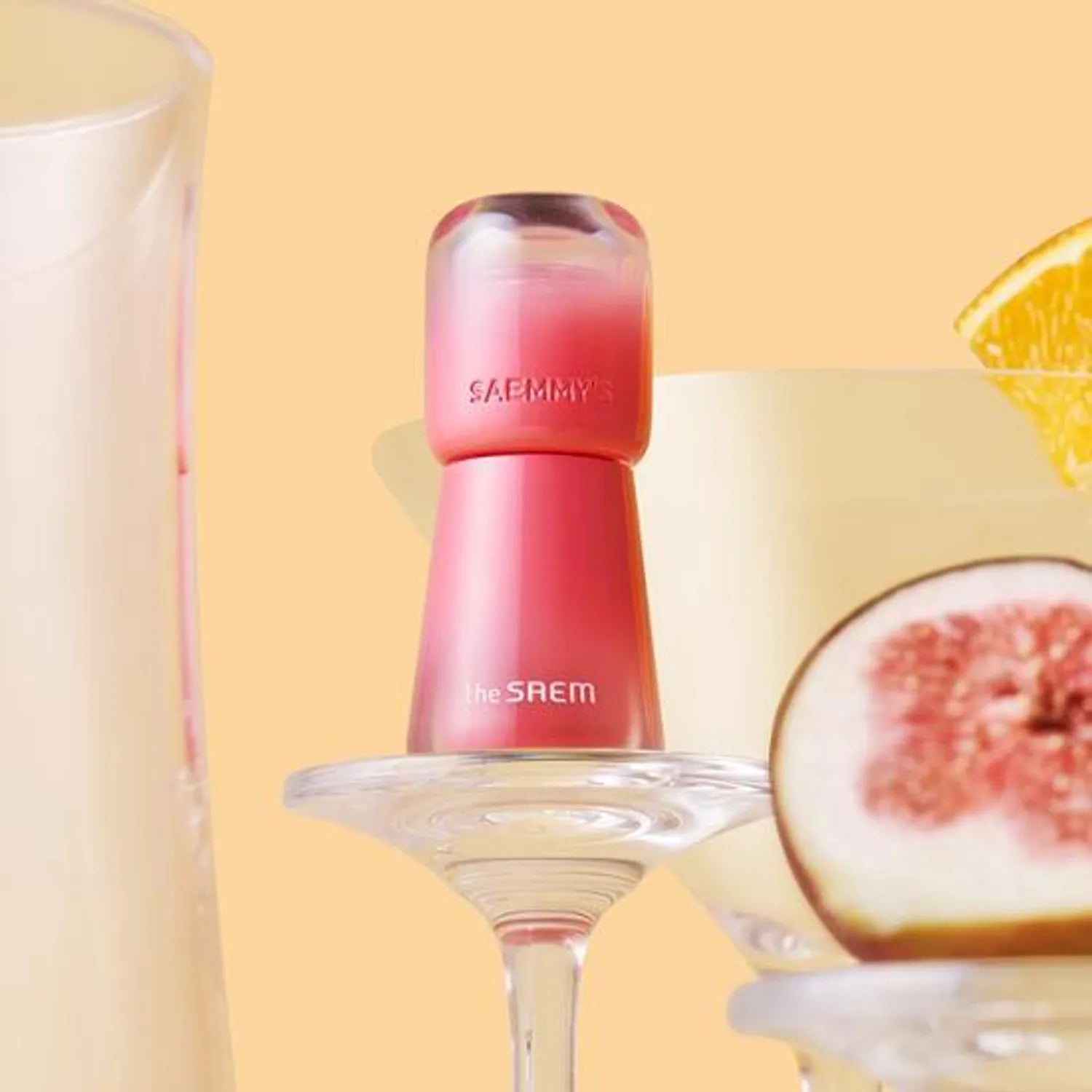 THE SAEM Saemmy's Aid Shot Tint de la marque The Saem, flacon rose en studio avec agrumes sur fond beige