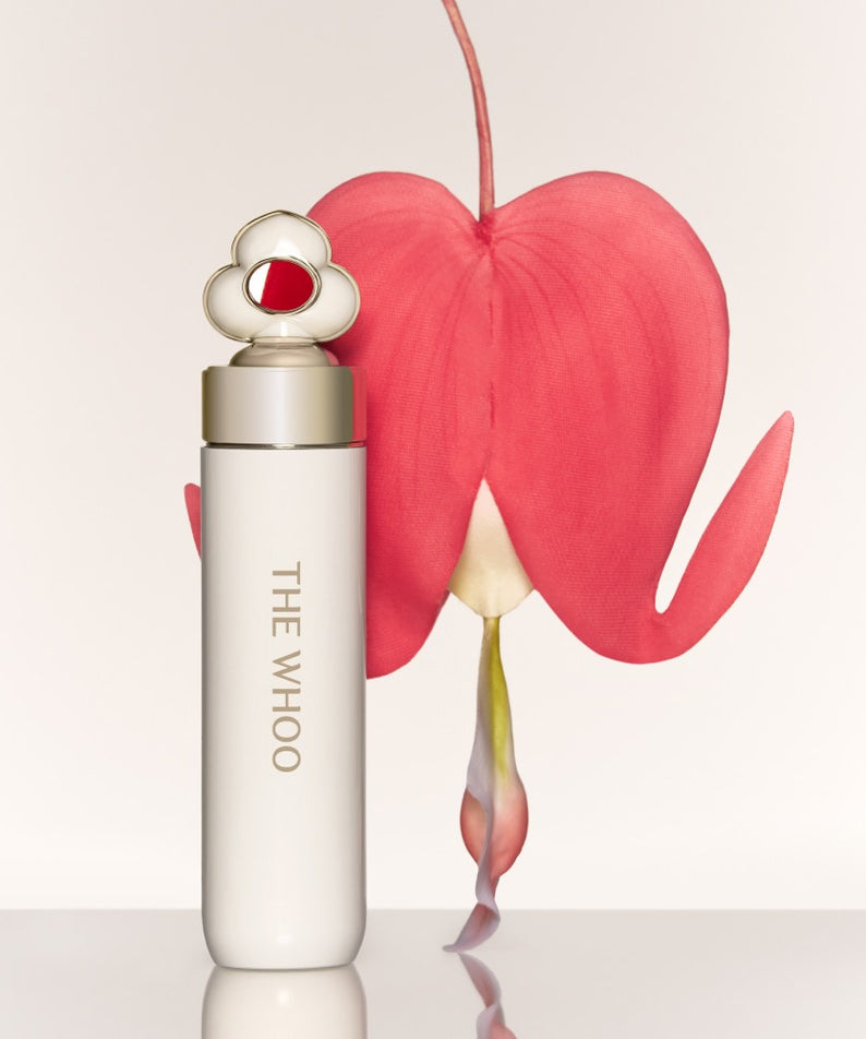 THE WHOO Essentail Lip Glow Balm de la marque THE WHOO, tube blanc sur fond clair, éclat et cœur rose rouge.