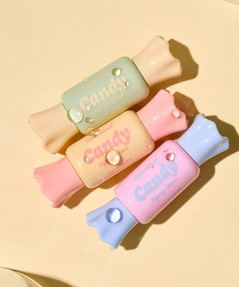 THE SAEM Saemmul Candy Syrup Gloss en quatre teintes pastel disposées artistiquement sur fond beige.