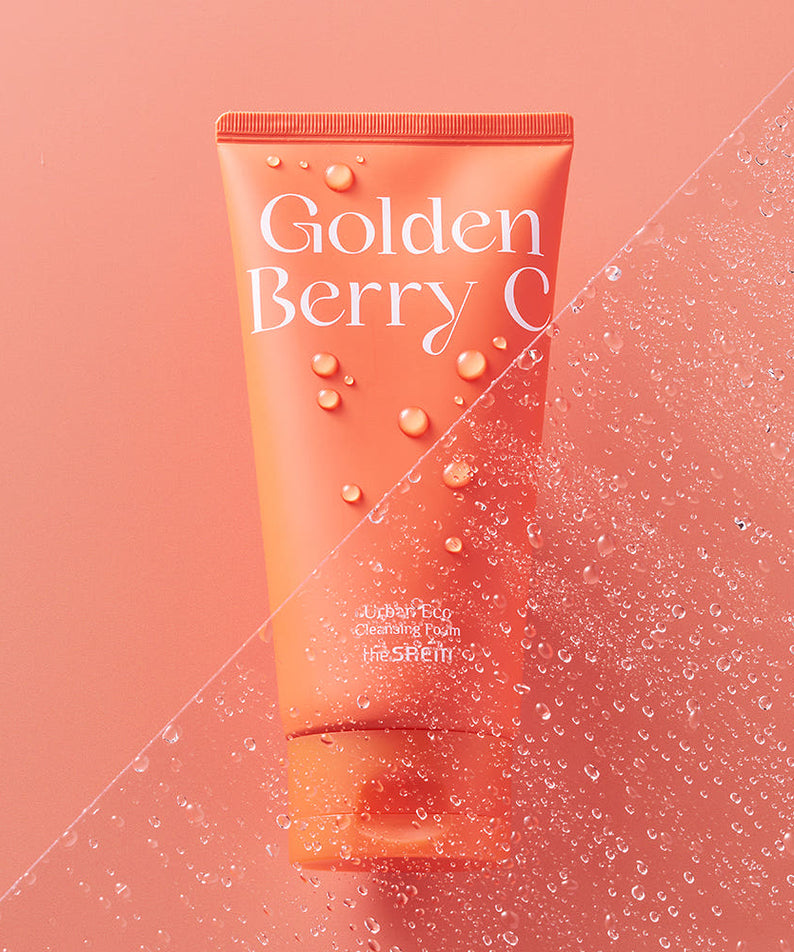 THE SAEM Urban Eco Golden Berry C Cleansing Foam 150ml en gros plan avec des gouttelettes d'eau sur fond corail.
