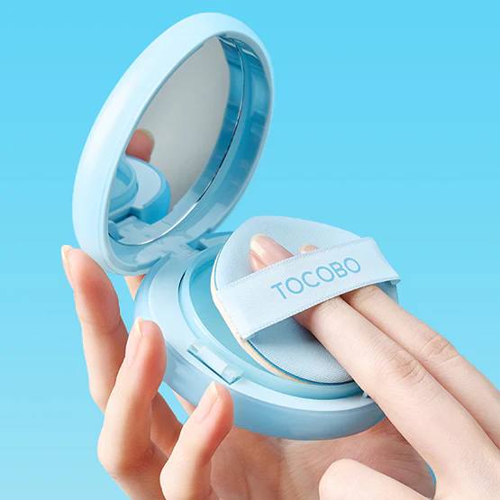 TOCOBO Blur Finish Sun Cushion, marque TOCOBO : coussin solaire bleu en packaging, tenue en main sur fond bleu ciel.