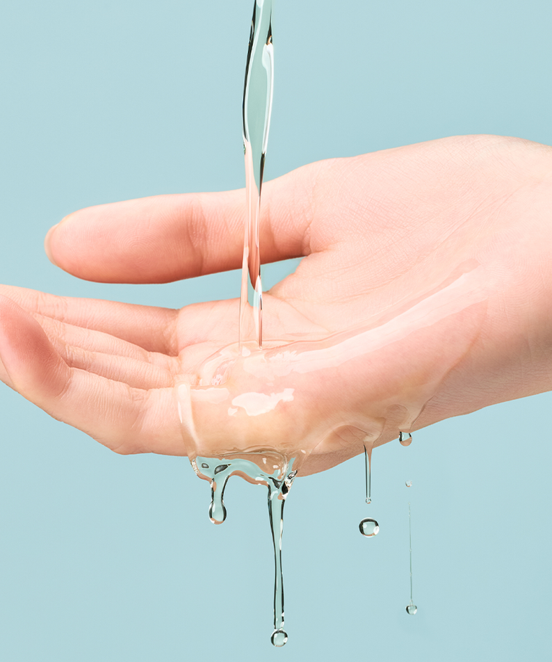 Main tenant le toner TOCOBO Cica Calming Aqua Toner avec liquide transparent coulant sur la peau, fond bleu. Soin du visage hydratant.