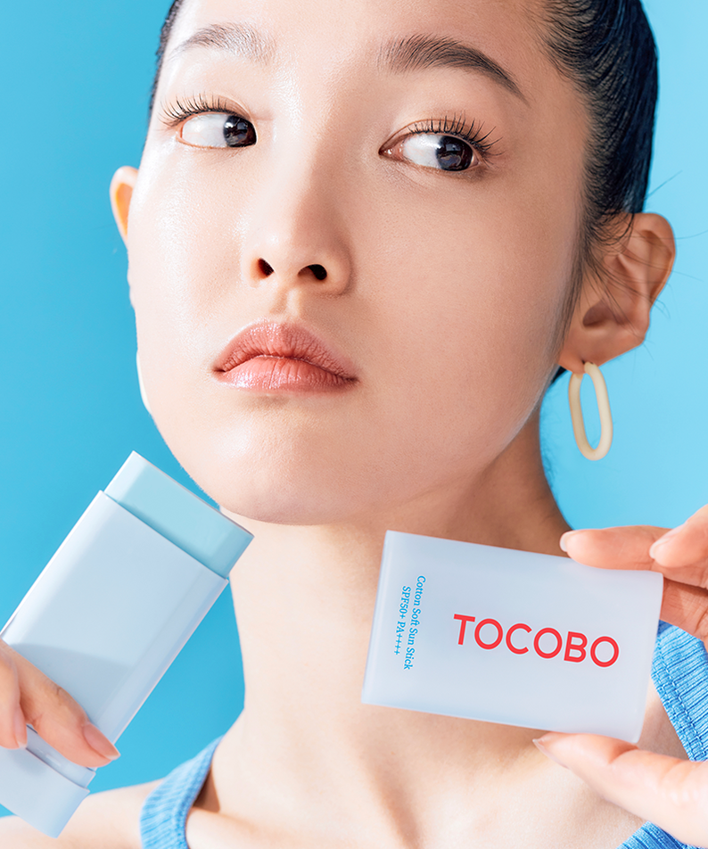 Personne utilisant le TOCOBO Cotton Soft Sun Stick, un écran solaire efficace et pratique, présenté sur fond bleu.