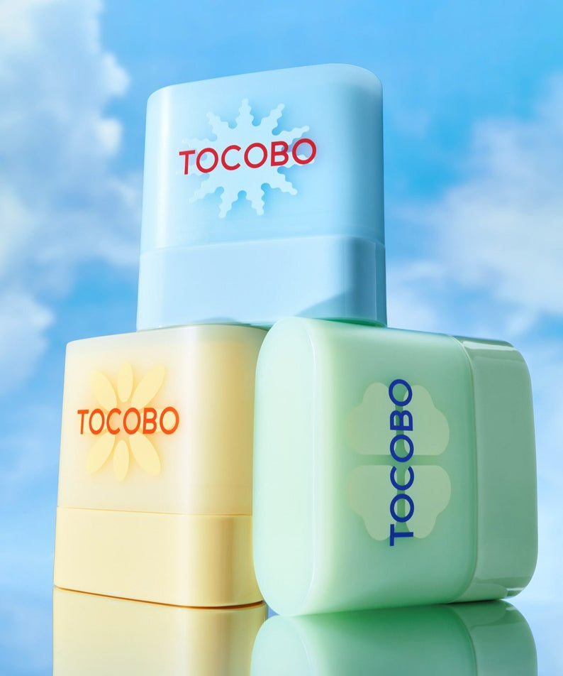 TOCOBO Mini Sun Stick Trio, produits TOCOBO sur fond ciel bleu, prise de vue studio, ambiance estivale