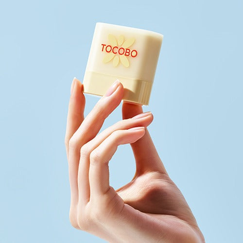 TOCOBO Mini Sun Stick Trio, main tenant un stick solaire TOCOBO sur fond bleu clair, photo produit en gros plan.