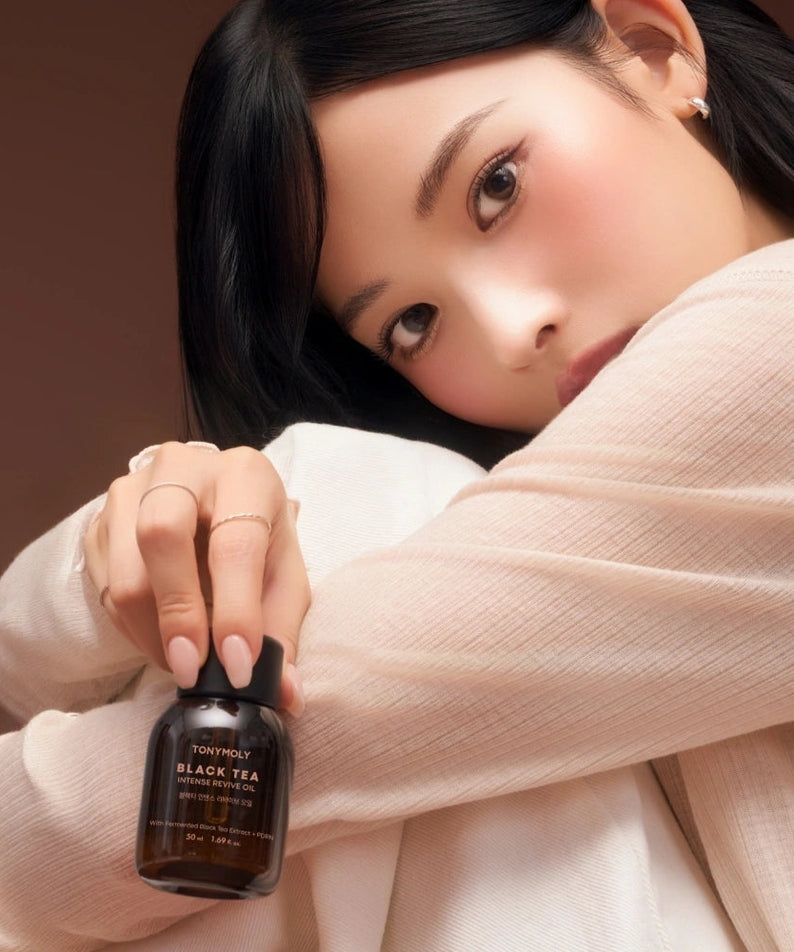 Décrivez l’image en français : TONY MOLY Black Tea Intense Revive Oil 50ml de la marque, flacon près d’un visage, ambiance spa.