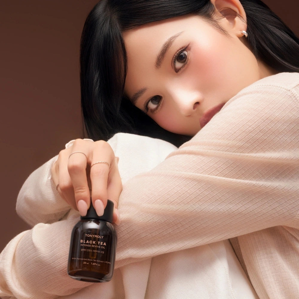 Décrivez l’image en français : TONY MOLY Black Tea Intense Revive Oil 50ml de la marque, flacon près d’un visage, ambiance spa.