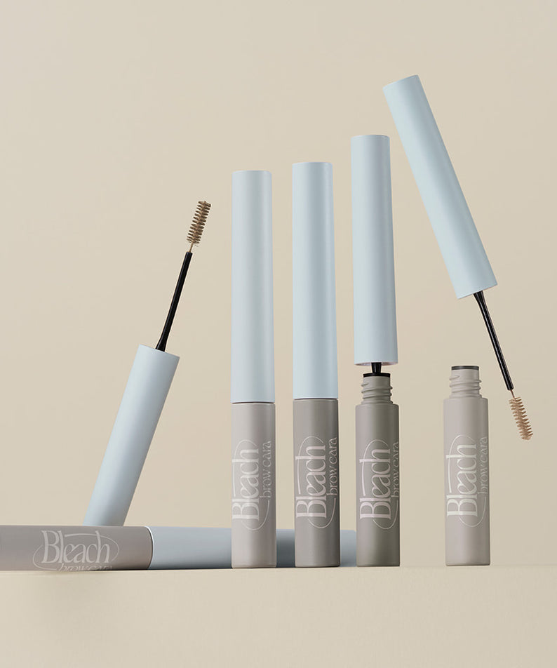 Décris l'image en français: TOO COOL FOR SCHOOL Bleach Brow Cara, tubes et brosses brow, produits sur fond clair.
