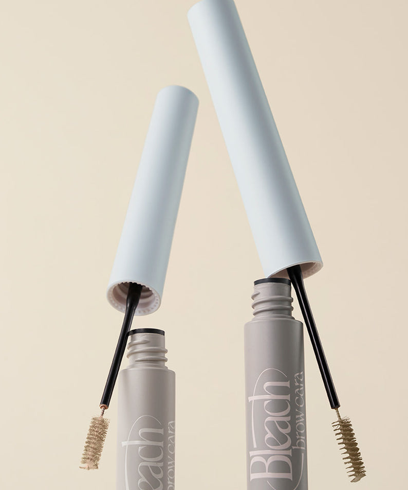 TOO COOL FOR SCHOOL Bleach Brow Cara, brosse à sourcils dans flacons gris sur fond beige clair, vue rapprochée.