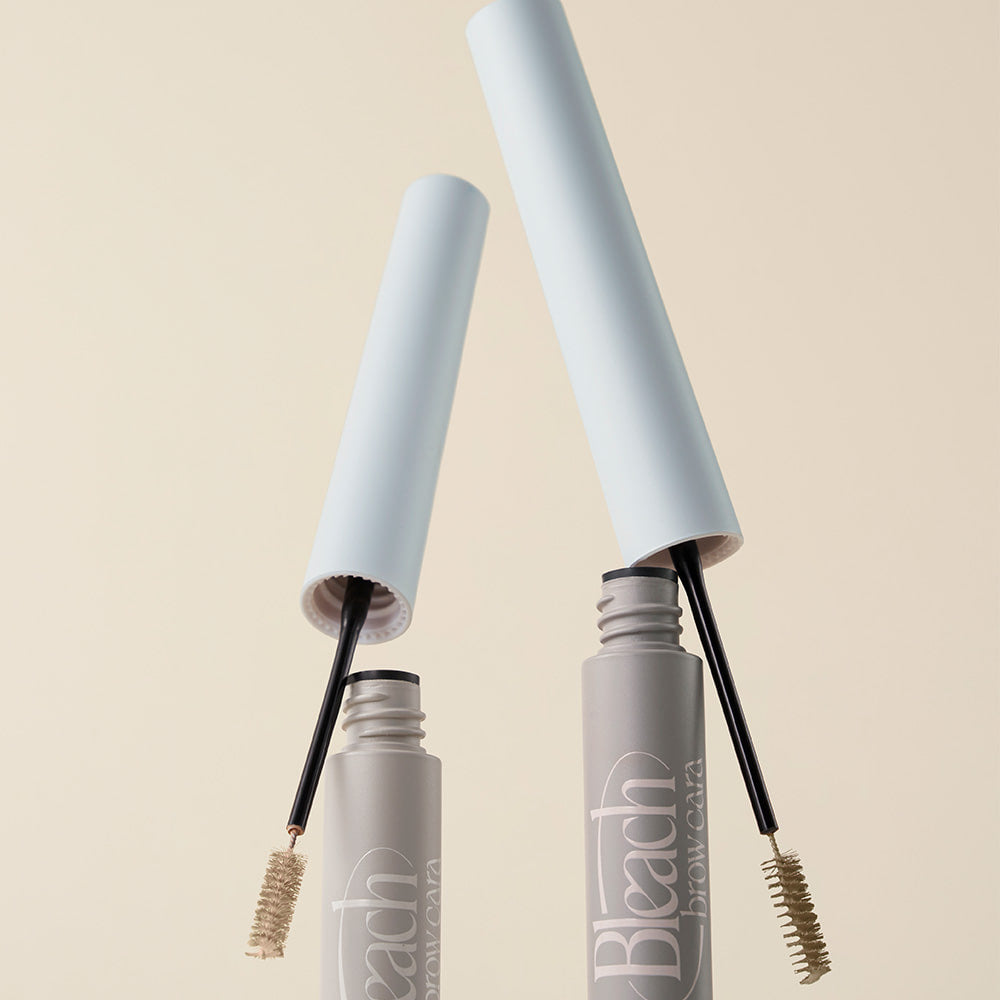 TOO COOL FOR SCHOOL Bleach Brow Cara, brosse à sourcils dans flacons gris sur fond beige clair, vue rapprochée.