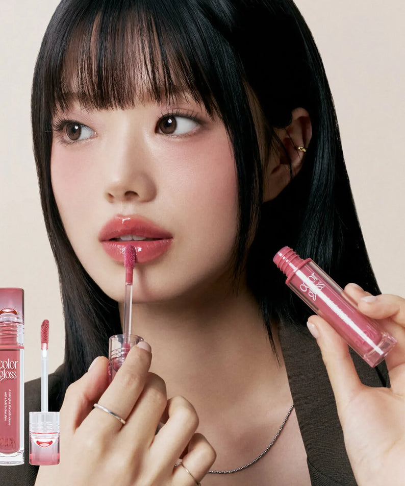 TOO COOL FOR SCHOOL Verre Color Gloss : femme maquillée appliquant le gloss rose, pack visible sur fond sombre