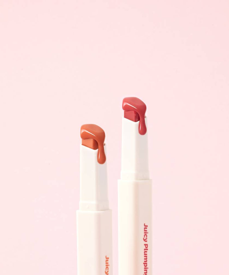 Deux rouges à lèvres TOUCH IN SOL Vegan Again Juicy Plumping Lipstick posés sur fond rose.