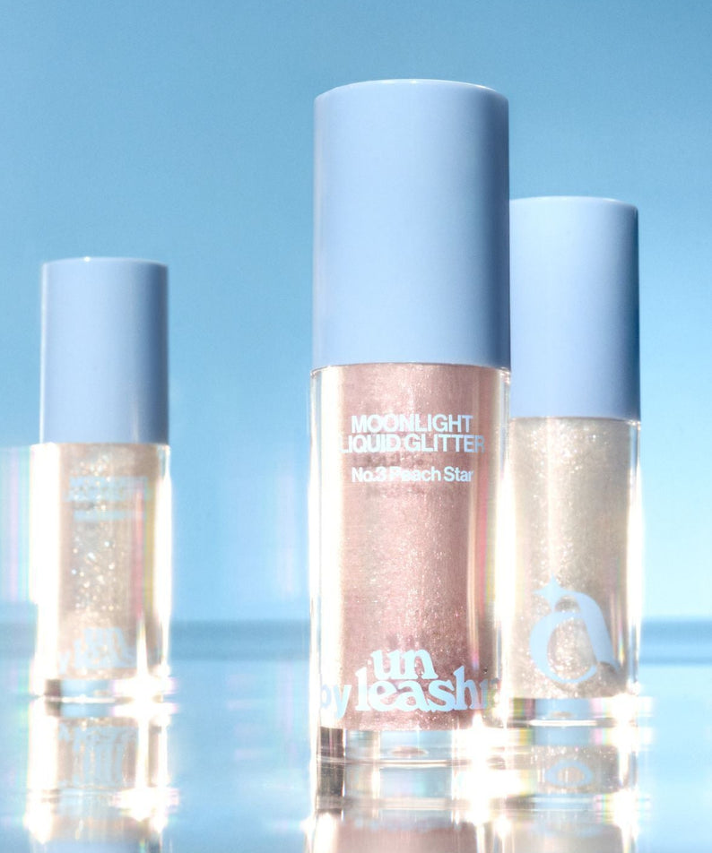 UNLEASHIA the Moonlight Liquid Glitter, flacons nacrés sur fond bleu ciel, éclat liquide scintillant de la marque UNLEASHIA.