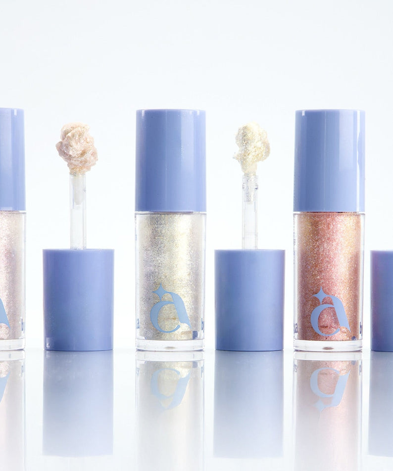 UNLEASHIA the Moonlight Liquid Glitter : flacons liquides pailletés bleu, or et rose sur fond blanc, décor lune.