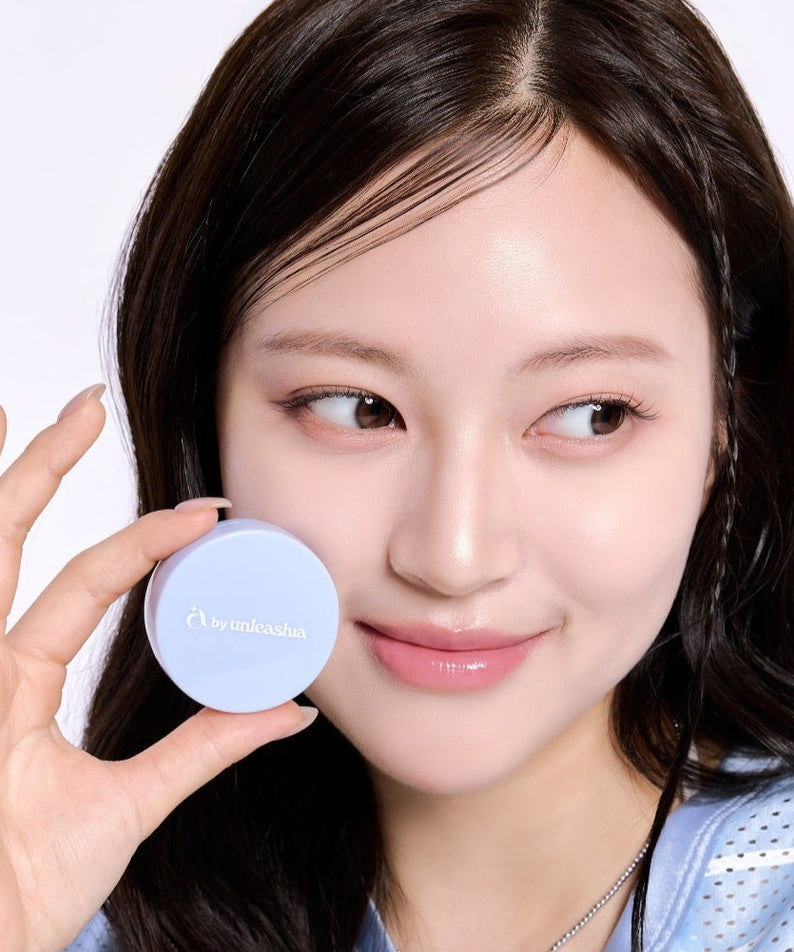 Femme souriante tenant la UNLEASHIA Be Be Blue Cushion, maquillage innovant pour une peau éclatante.