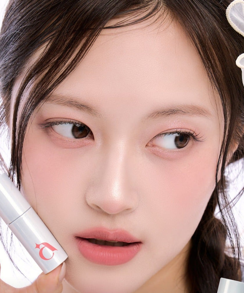 Jeune femme portant UNLEASHIA Clound Kiss Velvet Tint sur les lèvres, tenant le produit, avec un regard doux et sophistiqué.