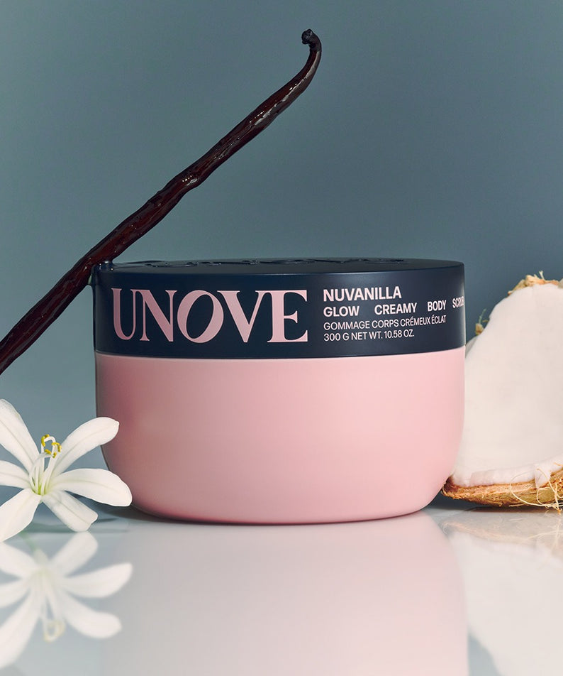 UNOVE Anove Glow Creamy Body Scrub 300g, marque UNOVE, pot rose sur fond bleu avec fleurs et noix de coco