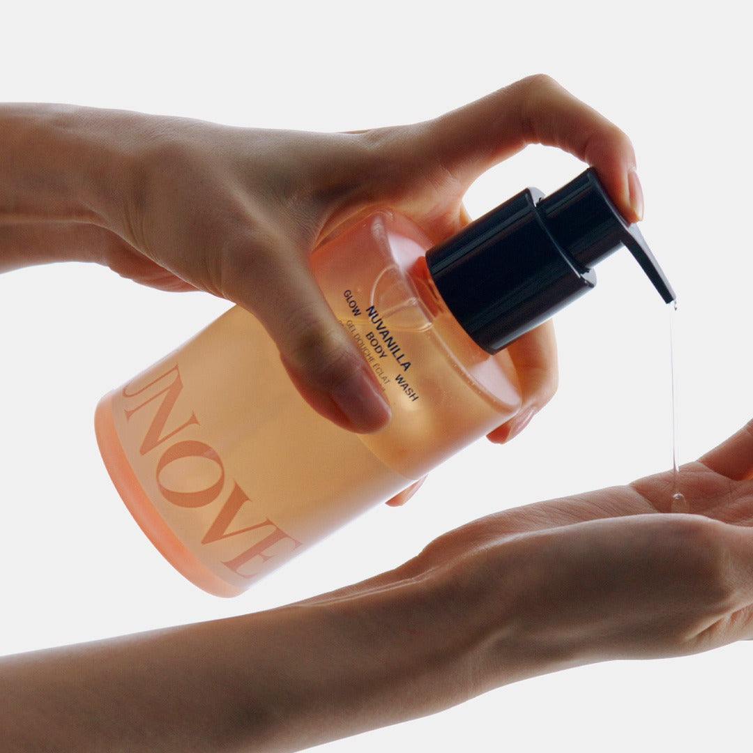 UNOVE Glow Body Wash 290ml, flacon en main, mains tenant le produit sur fond clair, contexte visuel maquillage