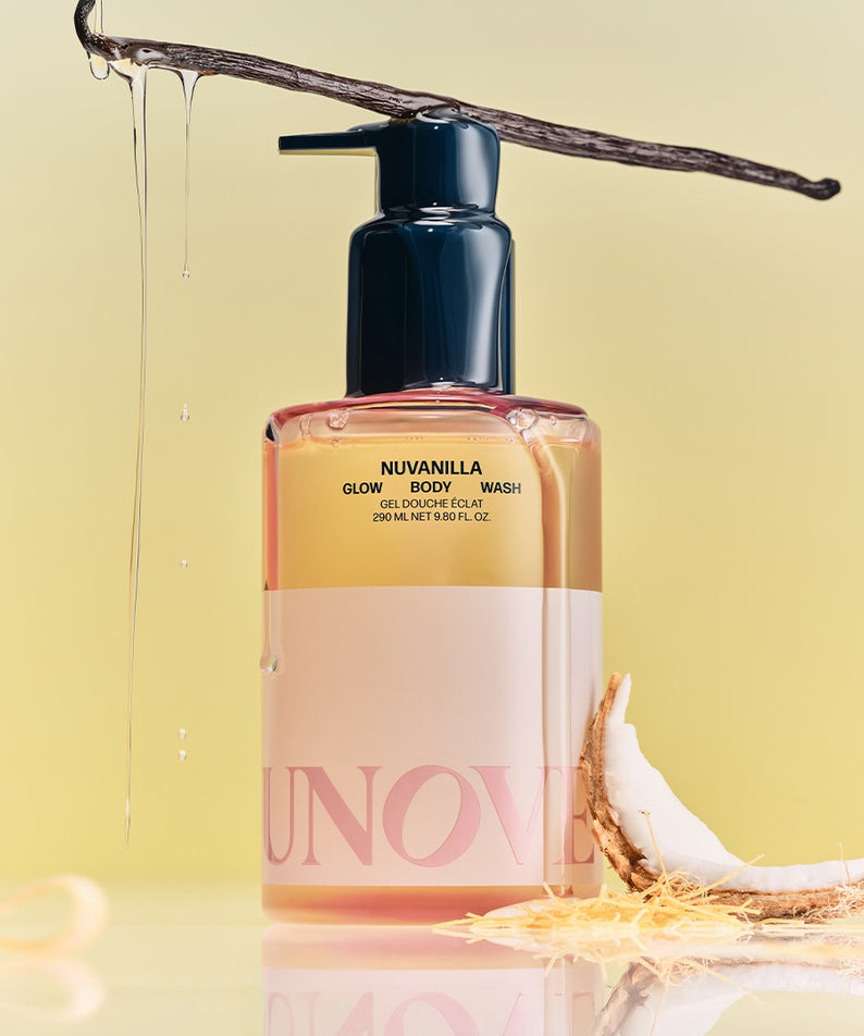Bouteille de UNOVE Anove Glow Body Wash 290ml entourée de vanille et noix de coco, posée sur un fond jaune clair.
