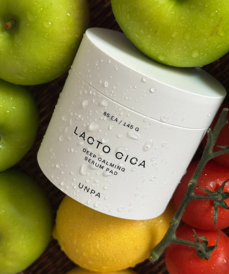 Décris l'image en français mentionnant UNPA Lacto Cica Deep Calming Serum Pad 85 Sheets, UNPA, sérum sur fond de fruits et légumes.