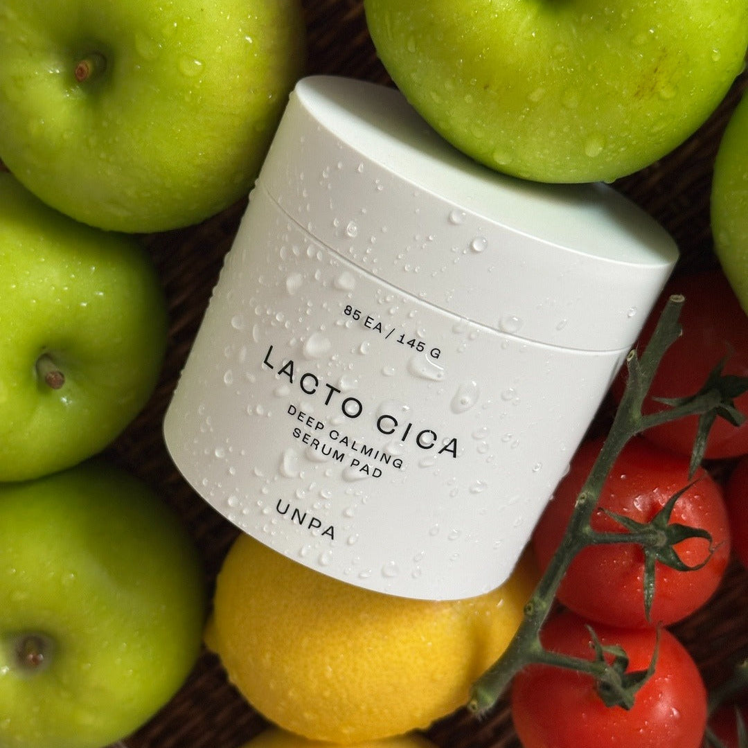 Décris l'image en français mentionnant UNPA Lacto Cica Deep Calming Serum Pad 85 Sheets, UNPA, sérum sur fond de fruits et légumes.