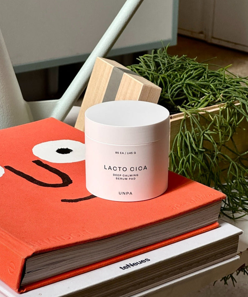 UNPA Lacto Cica Deep Calming Serum Pad 85 Sheets UNPA, pot sur livres et plante verte, ambiance salle de soins