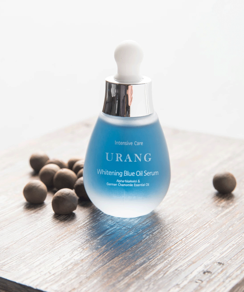Flacon de 30ml de URANG Brightening Blue Oil Serum sur une table en bois avec des noisettes autour.