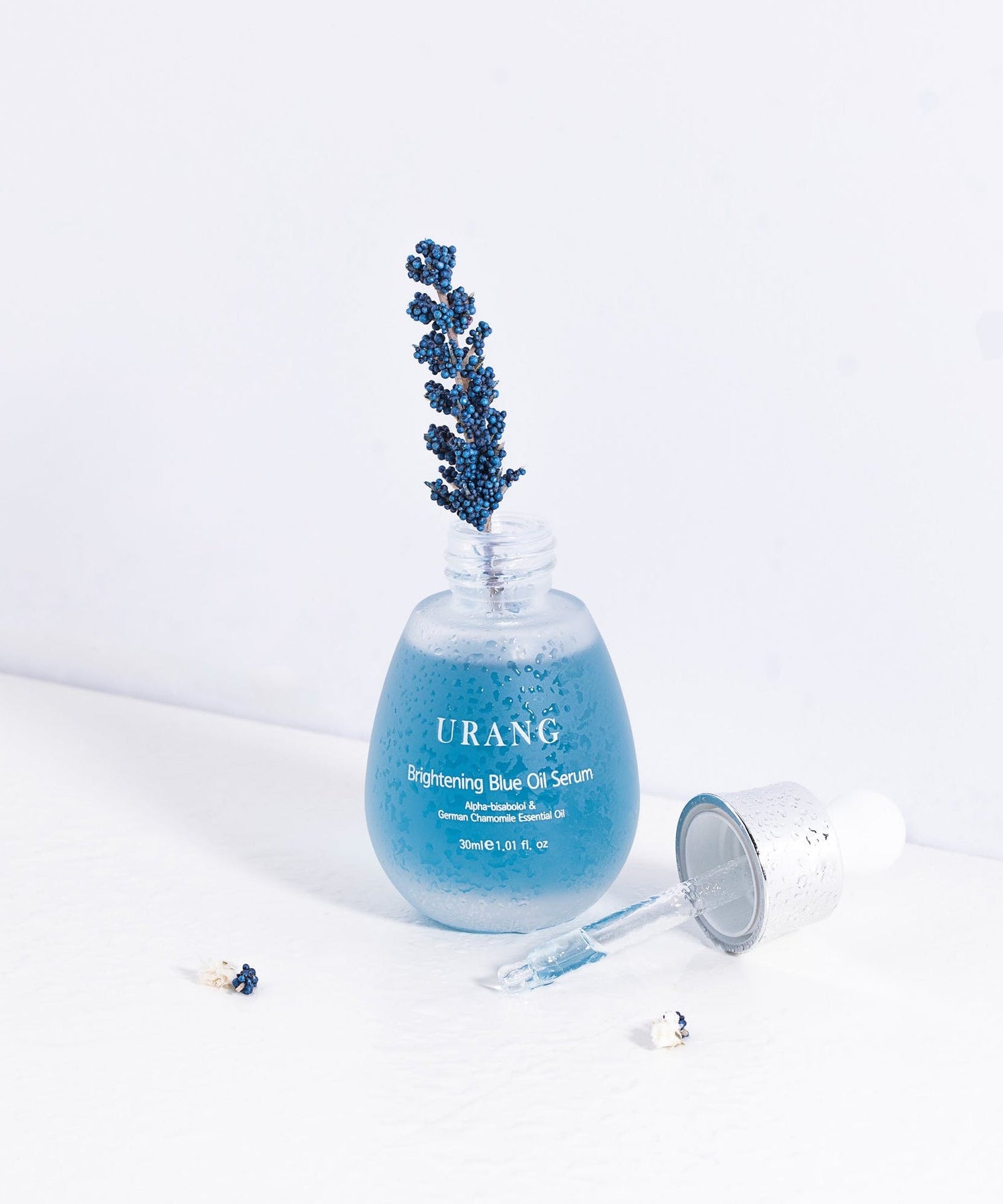 URANG Brightening Blue Oil Serum 30ml présenté avec gouttes et brindille sur fond blanc, sérum visage éclaircissant en huile bleue.