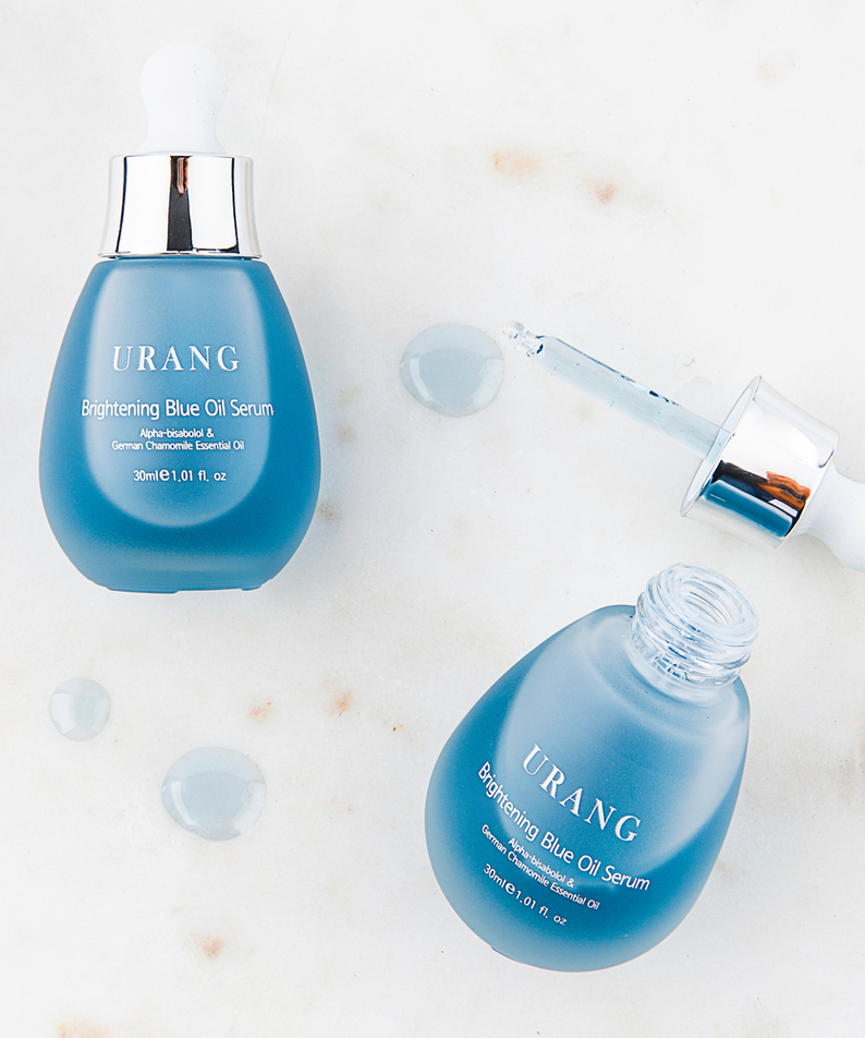 Flacons de URANG Brightening Blue Oil Serum 30ml sur fond marbré blanc, sérum bleu éclatant pour la peau, format 30ml, beauté visage.