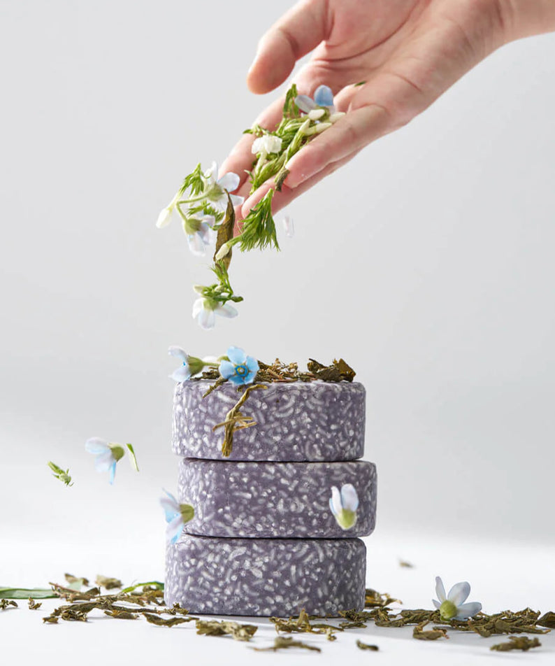 URANG Daily Oil Free Shampoo Bar empilés avec des herbes et des fleurs, illustrant un soin capillaire naturel et écologique.