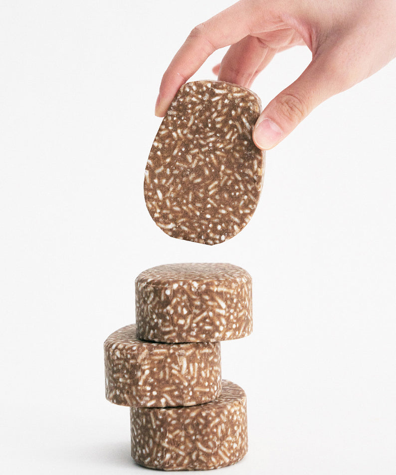 Main de tenant un URANG Mugwort Calming Shampoo Bar, empilés sur fond blanc, illustrant la texture et la forme uniques du produit.