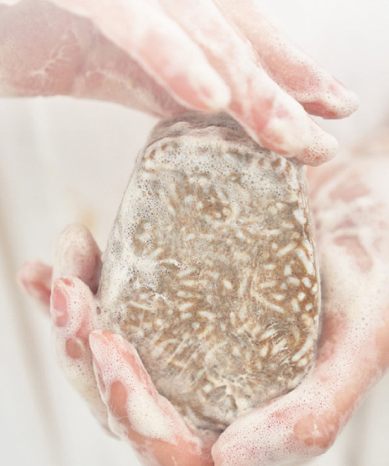 Barre de shampooing URANG Mugwort Calming entre des mains, apaisante et mousseuse, idéal pour des cheveux naturellement sains.