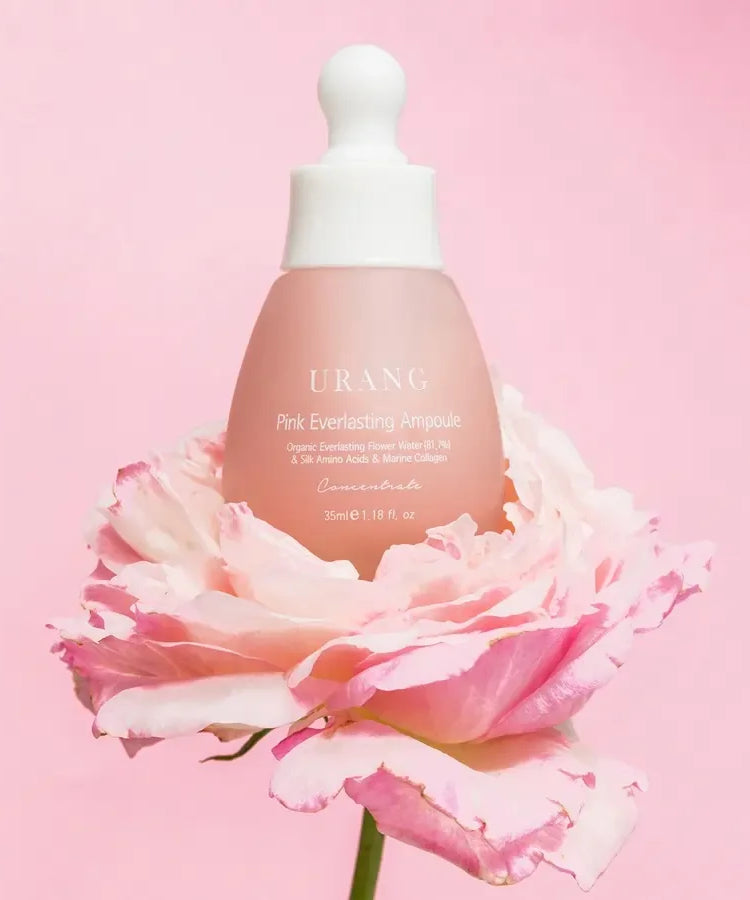 Flacon de l'URANG Pink Everlasting Ampoule posé sur une fleur rose, produit de soins de la peau coréen.