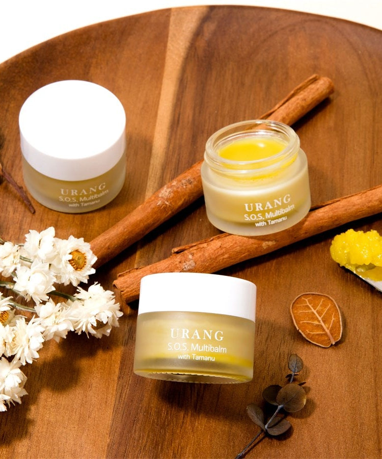 URANG SOS Multi Balm présenté sur un plateau en bois avec des ingrédients naturels, baume visible dans un pot ouvert. Soin hydratant tout-en-un.